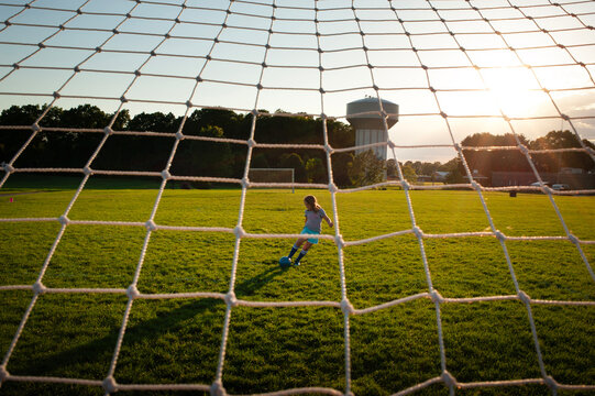 Young girl kicking soccer ball towards net sunny day
