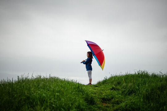 Side view tween girl holding coloful umbrella outdoors grey sky