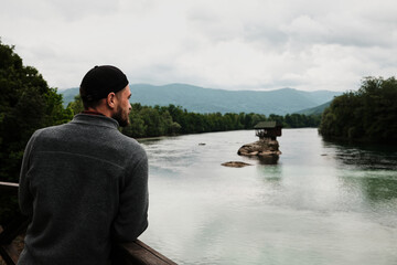 Man in a grey fleece jacket looking at the iconic house on the Drina River from a wooden viewpoint. Rear view. A popular tourist destination. Serbia country in spring season.