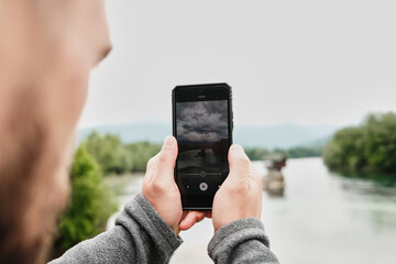 Close-up of a man filming the Drina River house on his phone, capturing the iconic Serbian view. Rear view. A popular tourist destination. Serbia country in spring season.