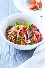 Simple salad with cherry tomatoes, red onion and fresh herbs. Bright wooden background. Close up.	