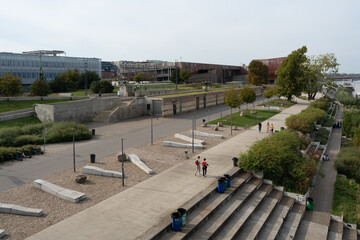 A wide view of the Vistula Boulevards in Warsaw, a modern public space for recreation. The landscape architecture features concrete promenades, benches, and green areas.