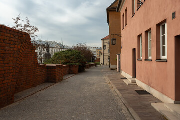 Obraz premium A cobblestone street slopes down alongside the historic brick fortification walls of Warsaw's Old Town, offering a view of the cityscape. A quiet path for tourism and sightseeing.