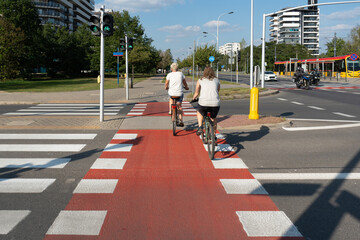 Cyclists ride on a dedicated red bike path in Warsaw, Poland. This illustrates modern urban...
