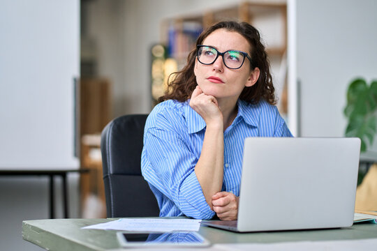 Serious professional business woman employee or student using laptop. Thoughtful lady looking away thinking of question or idea, working or learning on computer feeling doubt, at home or in office.