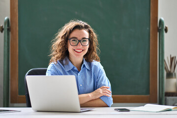 Portrait of young happy woman school professional online teacher or tutor sitting at desk with...