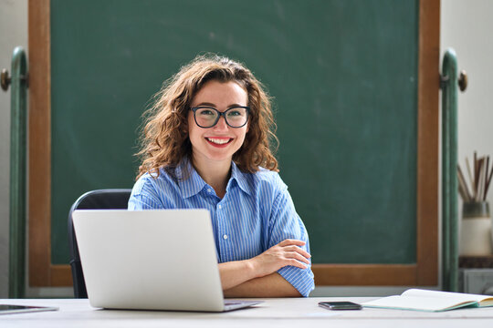 Portrait of young happy woman school professional online teacher or tutor sitting at desk with laptop computer, virtual distance classes for students, teaching remote education webinars concept.