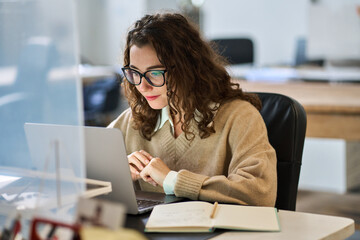 Plakat Busy young professional business woman employee or student wearing glasses using laptop watching online webinar or training web course, looking at computer, thinking, doing research working in office.