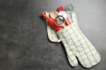 Different kitchen utensils in oven mitten on grey table, top view. Space for text
