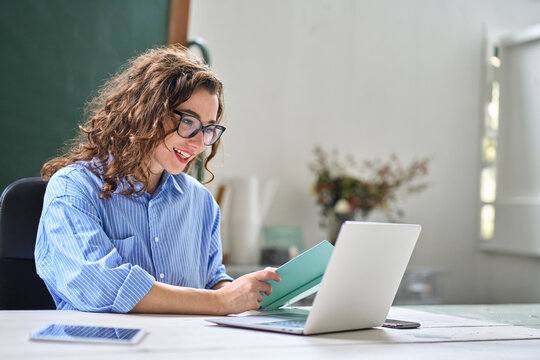 Young happy professional business woman online teacher or tutor sitting at work desk talking to student on video call teaching remote class webinar or distance web meeting on laptop computer.