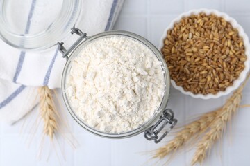 Wheat flour, grain and spikes on white tiled table, flat lay