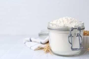 Wheat flour and spikes on white tiled table, closeup. Space for text