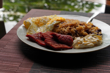 Close-up of a gallo pinto, a typical Costa Rican dish with rice, red beans, sausage, cream, and a fried egg.