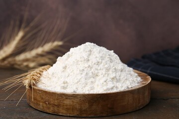 Wheat flour and spikes on wooden table, closeup