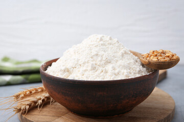 Wheat flour in bowl, grains and spikes on grey table, closeup