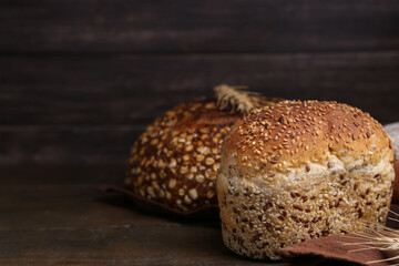 Freshly baked loaves of bread and spikes on wooden table, closeup. Space for text