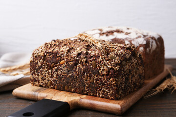 Freshly baked loaves of bread and spikes on wooden table against light background, closeup