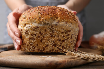 Woman with freshly baked bread at wooden table against grey background, closeup