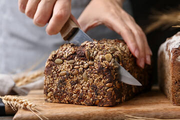 Woman cutting freshly baked bread at table, closeup