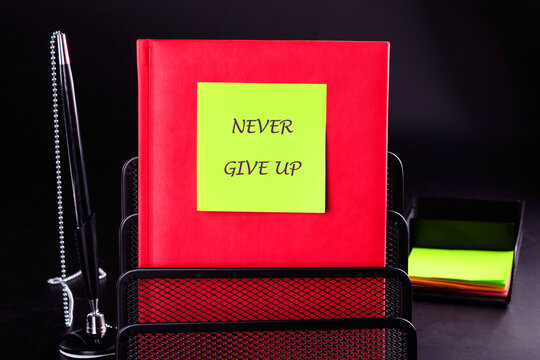 Naklejki Business development challenge concept and effort success idea. Never give up written on a green sticker on a red business book on a black background