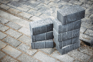Gray concrete bricks stacked on a construction site with textured surface and surrounding pavers