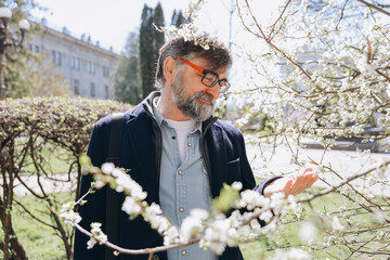 Senior man suffering from allergy to pollen near blooming tree