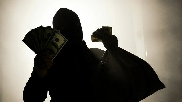 Mysterious silhouette of masked robber holding cash and bag filled with stolen money