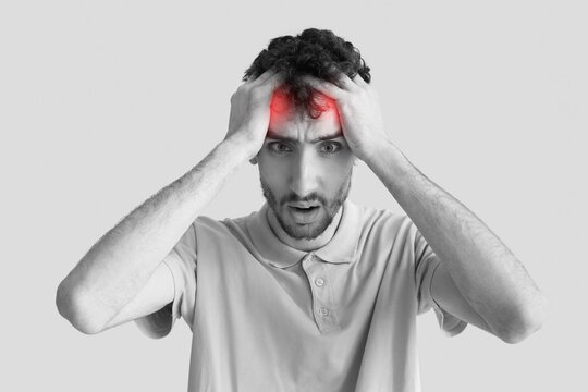 Young man suffering from headache on grey background