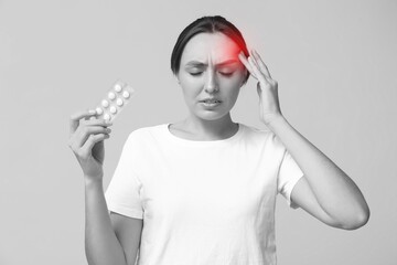 Young woman with pills suffering from headache on grey background