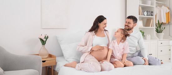 Cute little girl with her pregnant mother and father sitting in bedroom