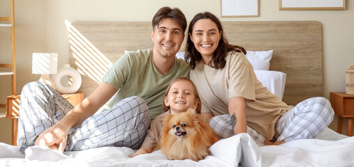 Happy little girl with her parents and Pomeranian dog sitting in bedroom
