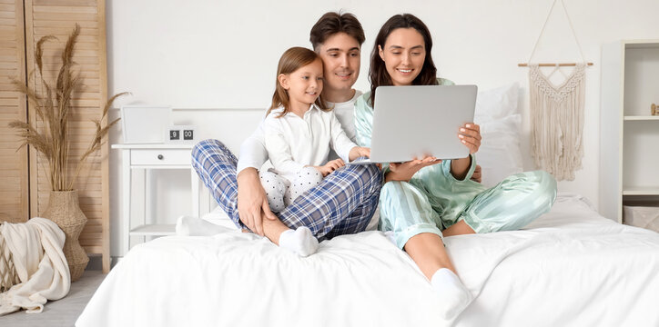 Little girl with her parents using laptop in bedroom