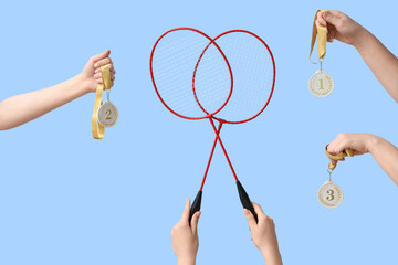 Female hands with badminton rackets and medals on blue background