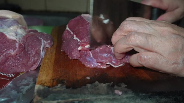 chopping raw beef meat on a chopping board. The meat is raw and has a lot of fat. Cooking preparation in the kitchen