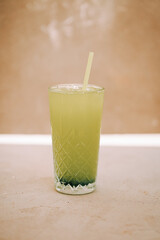Refreshing green beverage with a straw served in a textured glass on a beige background