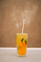 Refreshing yellow drink with mint and orange served in a tall glass on a simple background
