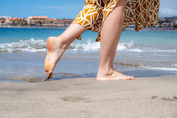 A woman is walking on the beach with her feet in the sand. The beach is calm and peaceful, and the woman seems to be enjoying her time