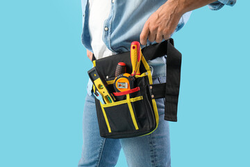 Male construction worker with measuring tape in tool belt on blue background, closeup