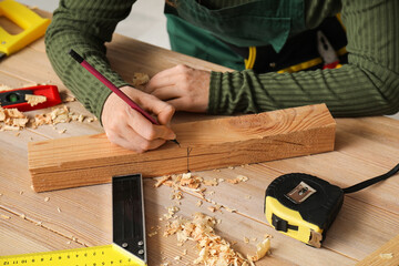 Female carpenter marking wooden plank with pencil in workshop