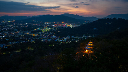 Aerial view of scenery Khao Rang viewpoint at twilight.
view of a town nestled among lush green mountains at sunset, with a Pavilion structure perched on the hillside at Phuket town at Dusk