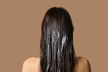 Young woman using cosmetics for hair treatment on beige background
