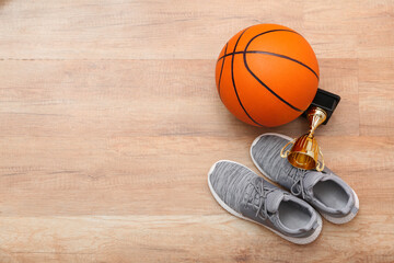 Ball for playing basketball, cup and shoes on wooden background