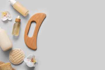 Composition with wooden guasha body massage tool, bottle of serum and reusable cotton pad on grey...