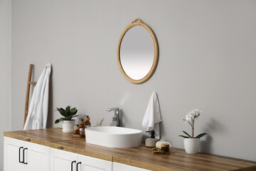 Modern sink, bath supplies on chest of drawers and mirror on light wall in bathroom
