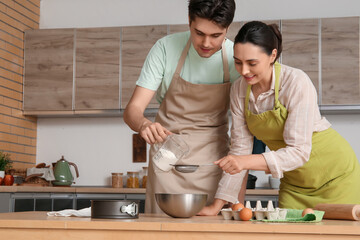 Happy young couple sifting flour in kitchen