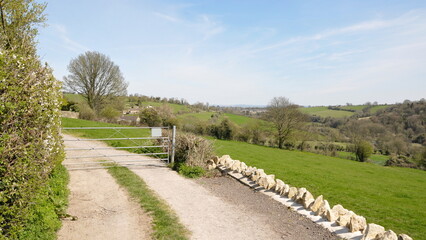 View of a country road through farmland fields and a closed metal access gate to a farm
