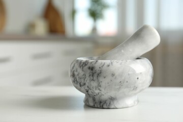 Mortar and pestle on white marble table in kitchen, closeup