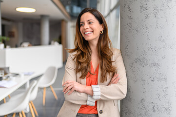 Portrait of smiling businesswoman with arms crossed smiling and looking away while standing by column in office
