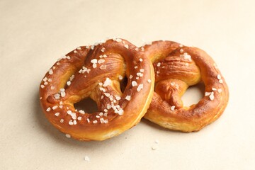Tasty pretzels with salt on beige background, closeup