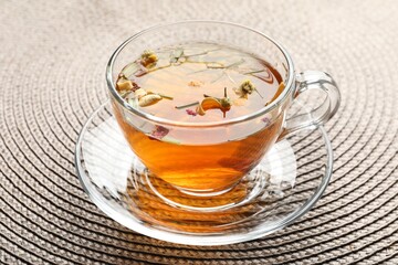 Aromatic herbal tea in glass cup on mat, closeup